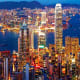 Hong Kong skyline at dusk with illuminated skyscrapers, Victoria Harbour, and mountains in background